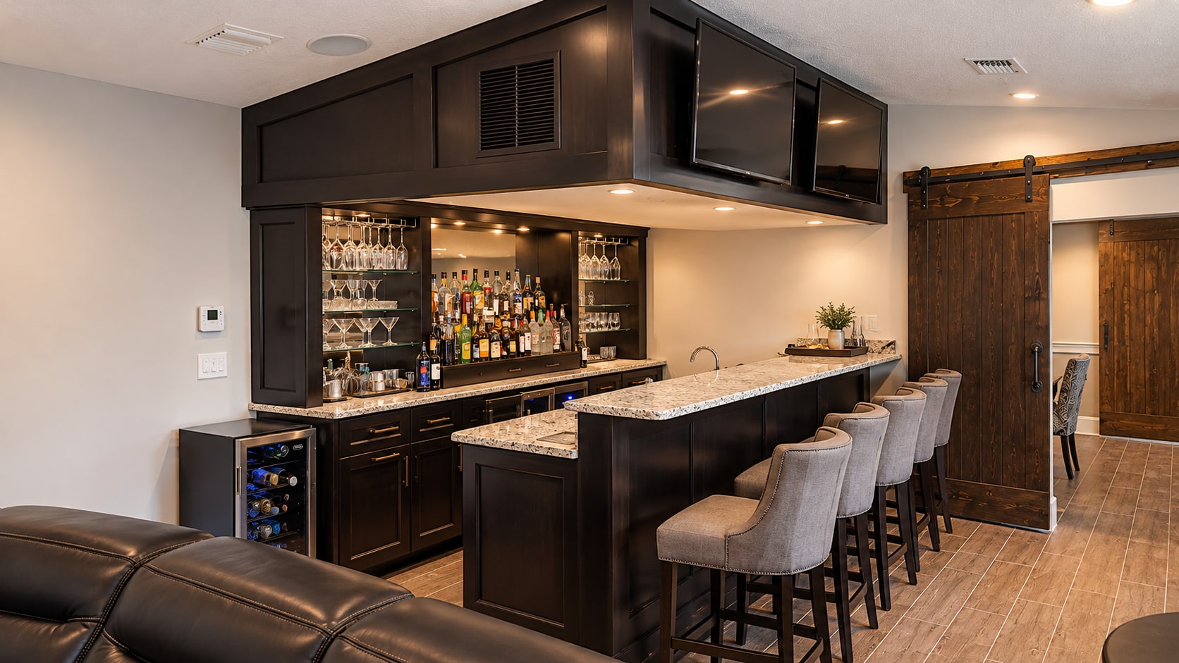 Dark custom bar with glass-front bottle storage, a stone serving island, and lounge seating